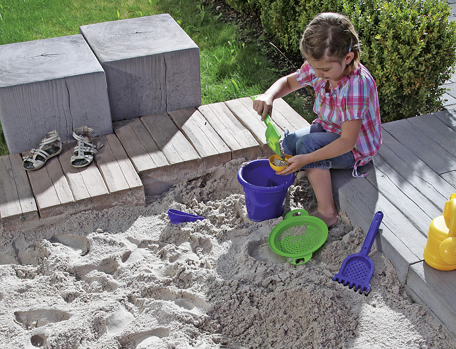 MAHORA TRIO und MAHORA Balken Holzstruktursteine MAHORA TRIO Holzstrukturstein, Farbe Meranti und MAHORA Balken, Holzstrukturstein kombiniert zu einem Sandkasten in dem ein Kind spielt